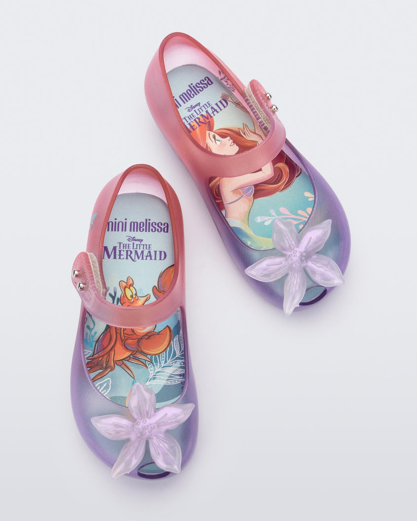 Top view of a pair of transparent pink and purple Mini Melissa Ultragirl + Disney Little Mermaid flats with a pearly white flower on top