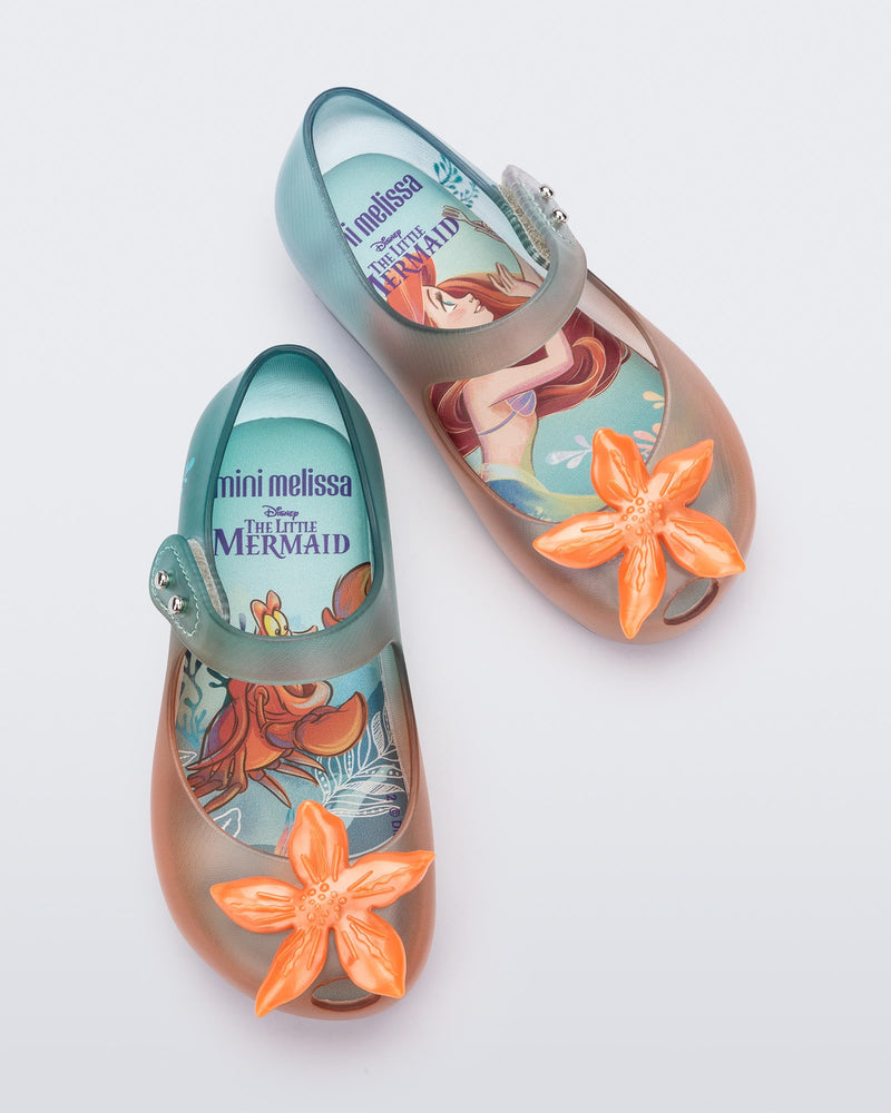Top view of a pair of transparent green and orange Mini Melissa Ultragirl + Disney Little Mermaid flats with a pearly orange flower on top