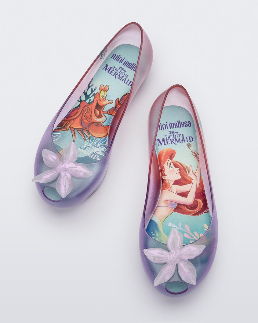 Top view of a pair of clear pearly pink and purple Mini Melissa Ultragirl + Disney Little Mermaid flats with a pearly purple flower.