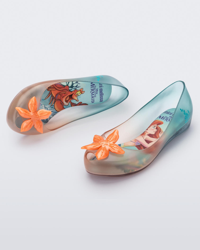 Angled view of a pair of transparent green and orange Mini Melissa Ultragirl + Disney Little Mermaid flats with a pearly orange flower on top