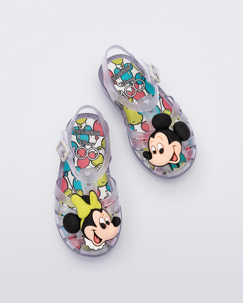 Top view of a pair of clear glitter Mini Melissa Possession + Disney 100 sandal with Mickey on one foot and Minnie on another foot.
