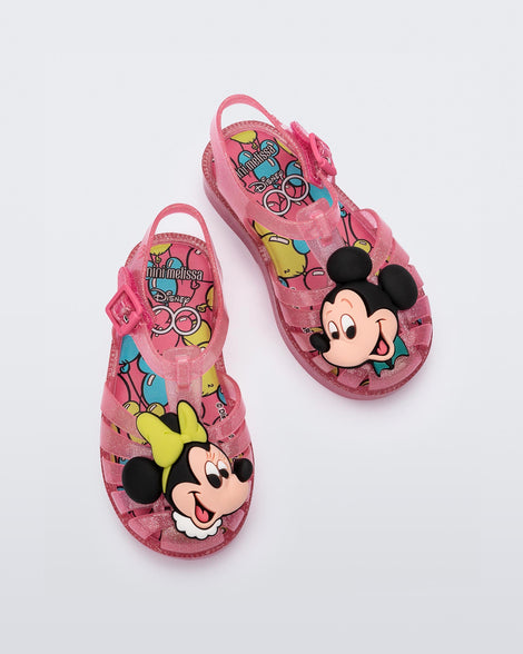 Top view of a pair of clear pink glitter Mini Melissa Possession + Disney 100 sandal with Mickey on one foot and Minnie on another foot.