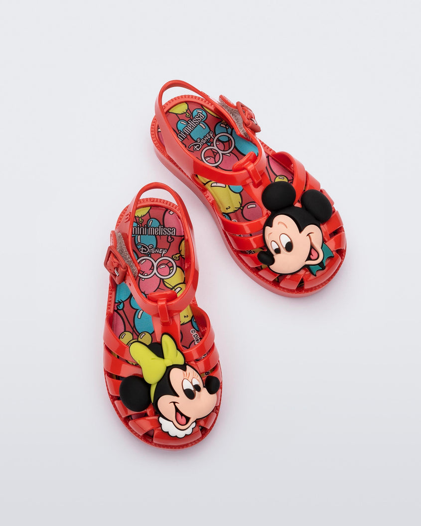 Top view of a pair of red Mini Melissa Possession + Disney 100 sandal with Mickey on one foot and Minnie on another foot.
