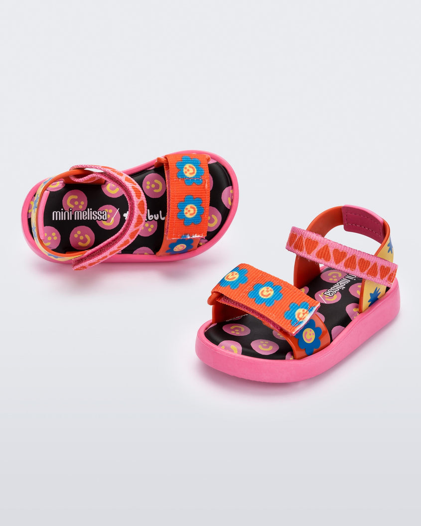 Angled view of a pair of pink, red, blue and yellow patterned Mini Melissa Pula Pula + Fabula sandals.