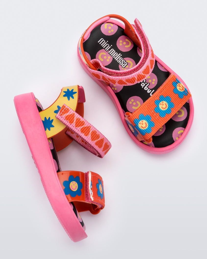 Top and side view of a pair of pink, red, blue and yellow patterned Mini Melissa Pula Pula + Fabula sandals.