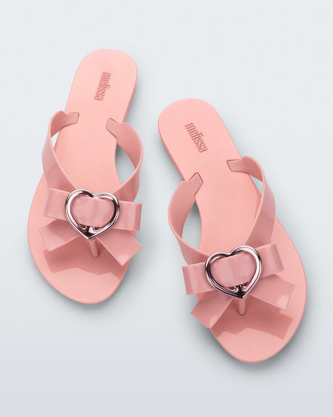 Top view of a pair of pink Melissa Harmonic Heart flip flops with a pink bow and metallic pink heart detail on the straps