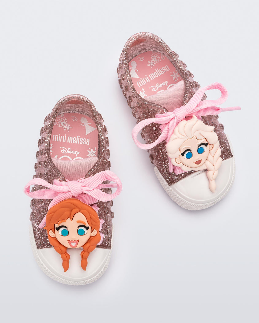 Top view of a pair of baby glitter pink Melissa Polibolha sneakers with a white toe top and Disney Frozen's Anna on the left and Elsa on the right.