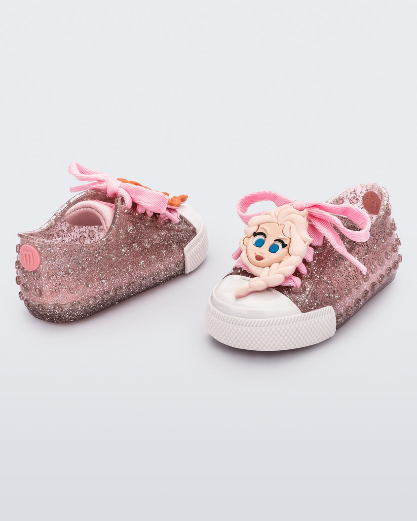 Angled view of a pair of baby glitter pink Melissa Polibolha Disney sneakers with a white toe top with Disney Frozen's Anna and Elsa.