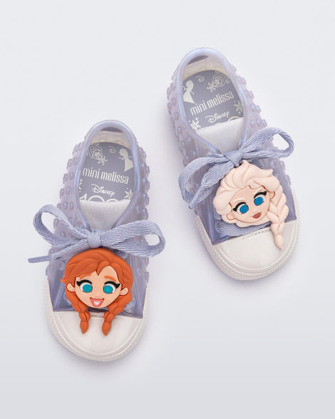 Top view of a pair of baby metallic blue Melissa Polibolha sneakers with a white toe top and Disney Frozen's Anna on the left and Elsa on the right.