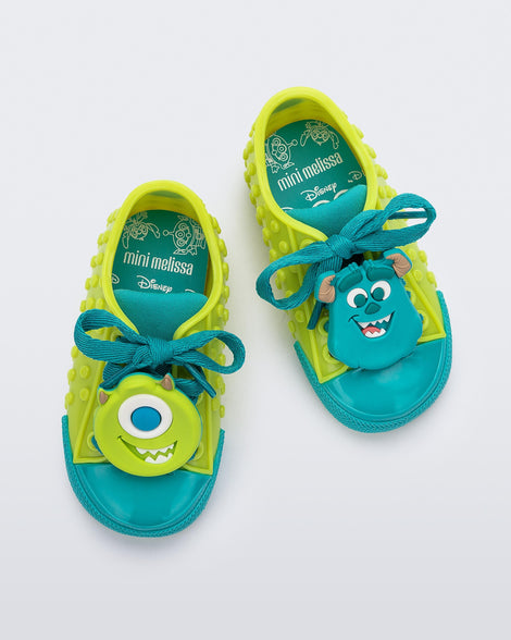 Top view of a pair of baby green Melissa Polibolha sneakers with a blue toe top and Disney Monsters Inc Mike on the left and Sully on the right.