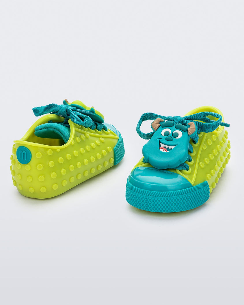 Angled view of a pair of baby green Melissa Polibolha Disney sneakers with a blue toe top with Disney Monsters Inc Mike and Sully.