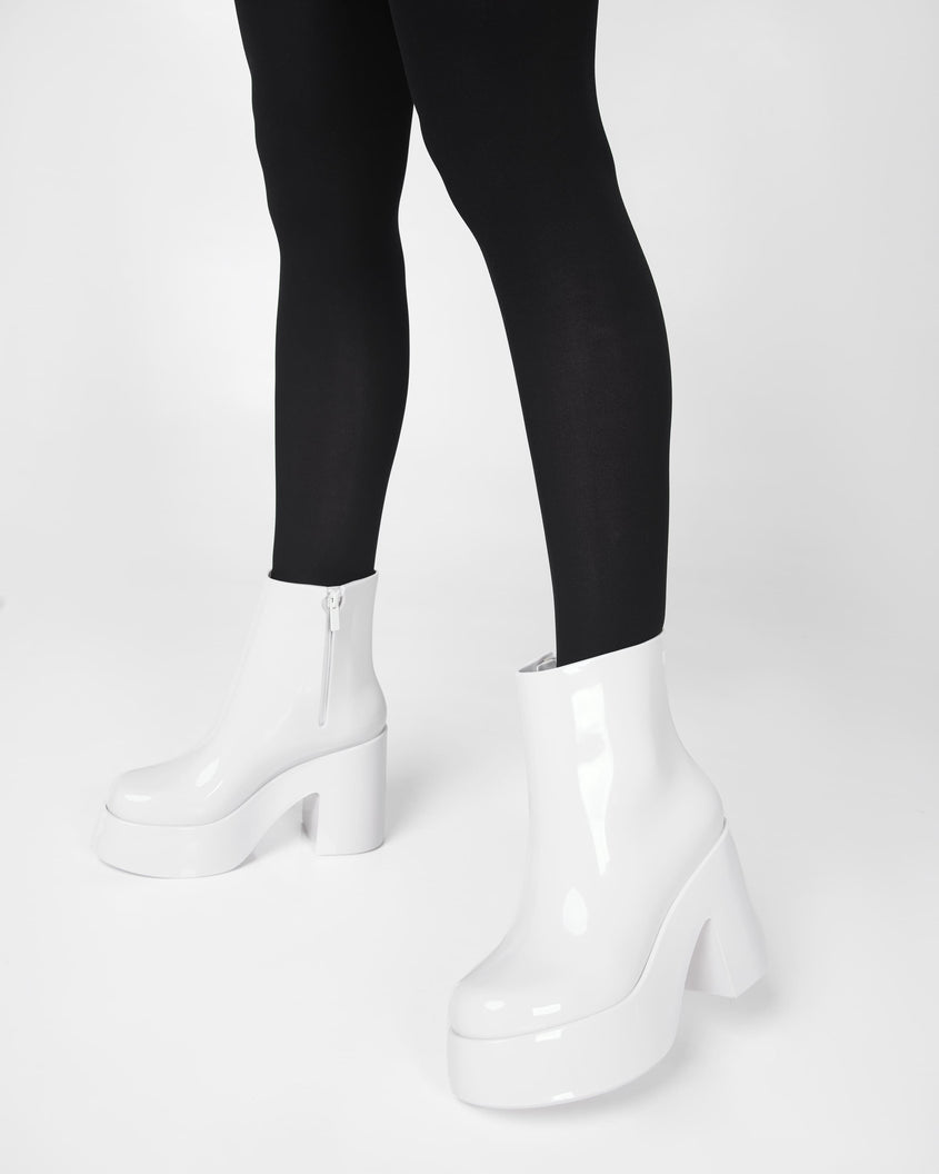 A model's legs in black pants wearing a pair of white Melissa Nubia platform heel boots.