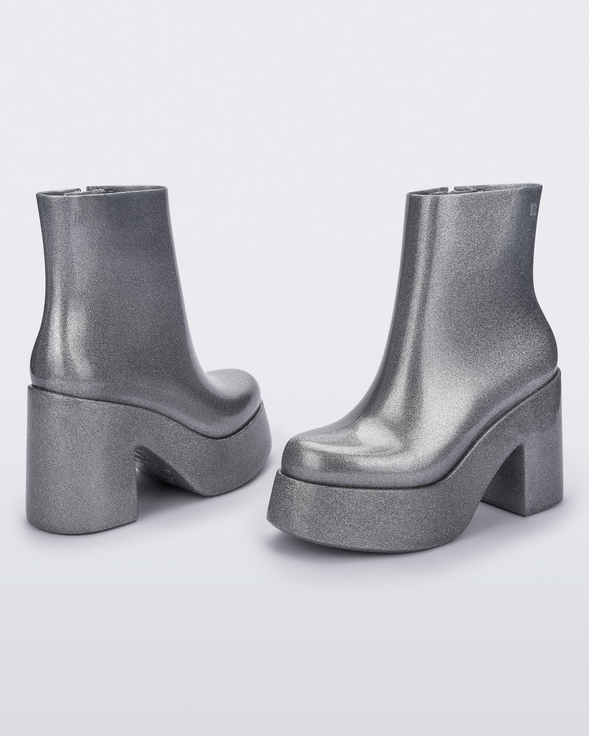 Angled and back view of a pair of silver glitter Melissa Nubia  platform heel boots.