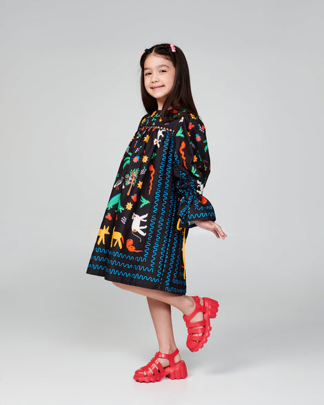 Child model in a black patterned dress wearing a pair of red Megan heeled sandals