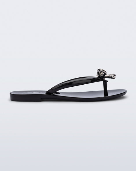 Side view of a black Harmonic Iris flip flop with silver bow