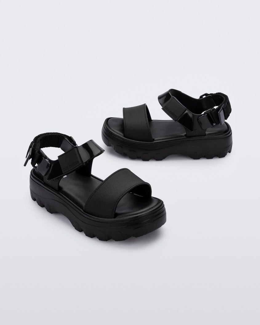 Angled view of a pair of Mini Melissa Kick Off platform sandals in black with adjustable velcro ankle straps 