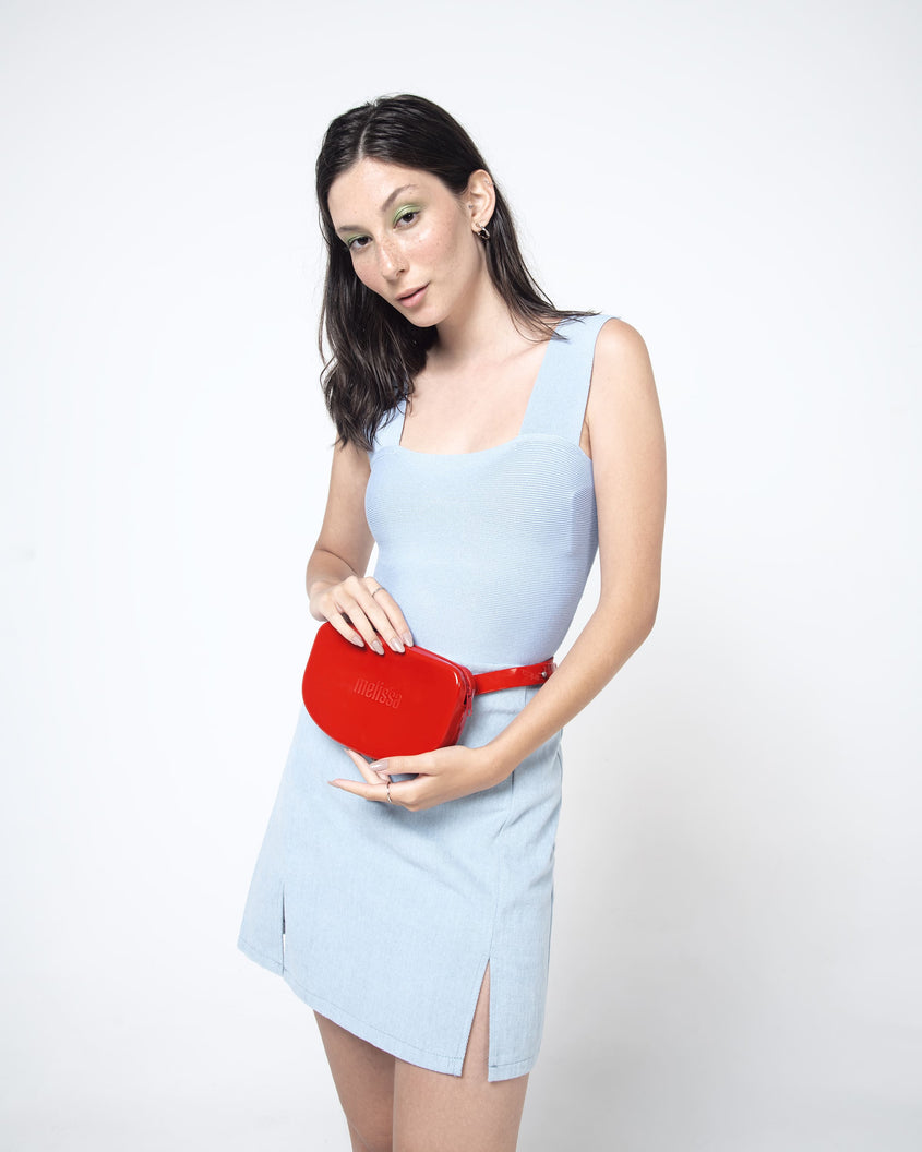 Model wearing a light blue dress and holding the red Melissa Go Easy bag.