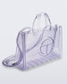 Angled view of a clear Melissa Large Jelly Shopper + Telfar bag with handles and a body strap