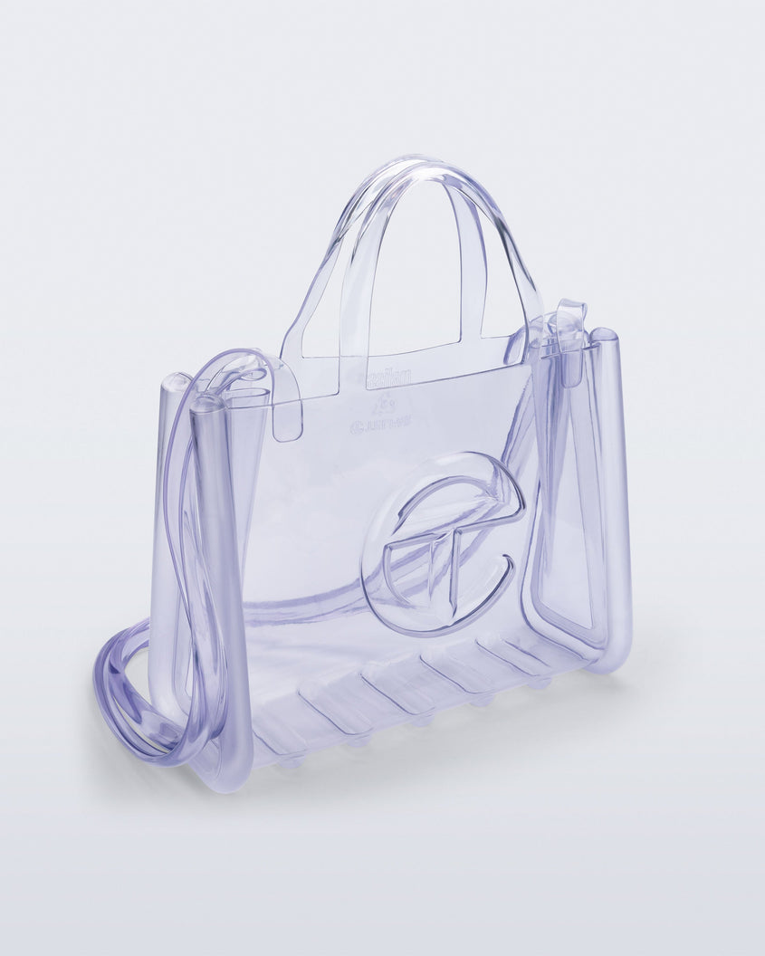 Angled view of a clear Melissa Medium Jelly Shopper + Telfar bag with handles and a body strap