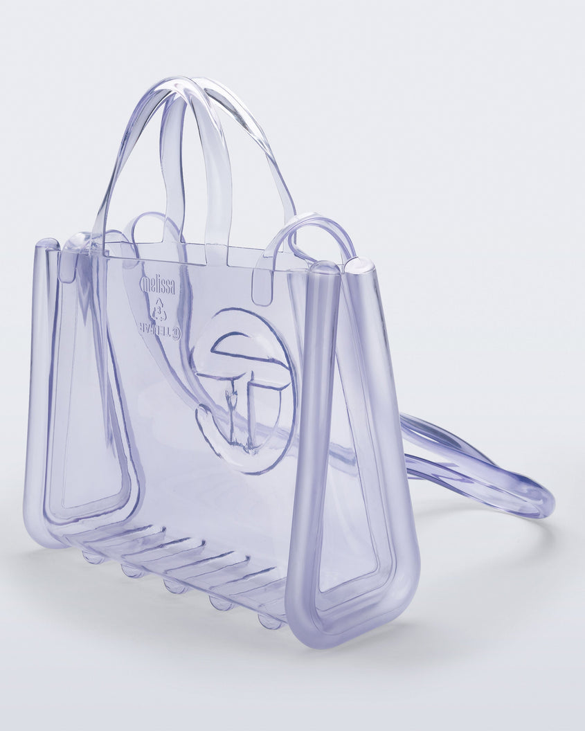 Angled view of a clear Melissa Medium Jelly Shopper + Telfar bag with handles and a body strap