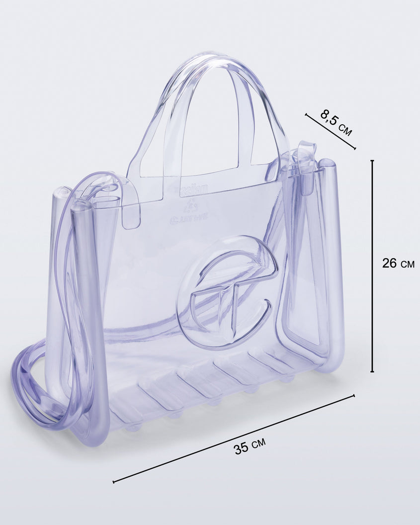 Angled view of a clear Melissa Medium Jelly Shopper + Telfar bag with handles and a body strap with dimensions 35 cm length, by 8.5 cm width, 26 cm height.