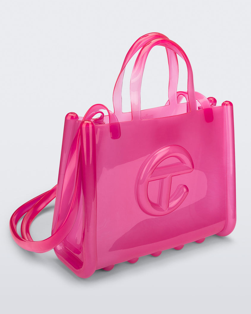 Angled view of a pink medium Melissa Jelly Shopper bag + Telfar bag with a handle and straps.