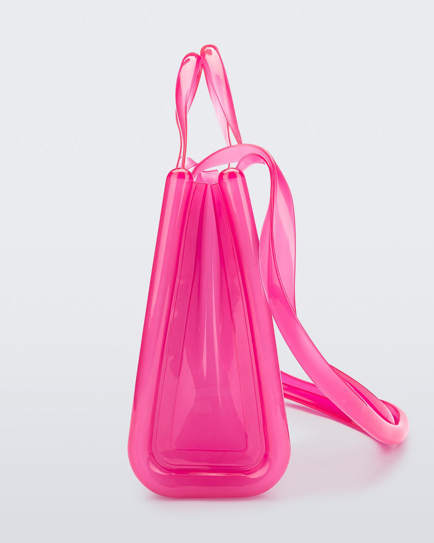 Side view of a pink medium Melissa Jelly Shopper bag + Telfar bag with a handle and straps.