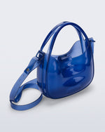 Angled view of a clear blue Mirror bag with cross body straps two clear handles.