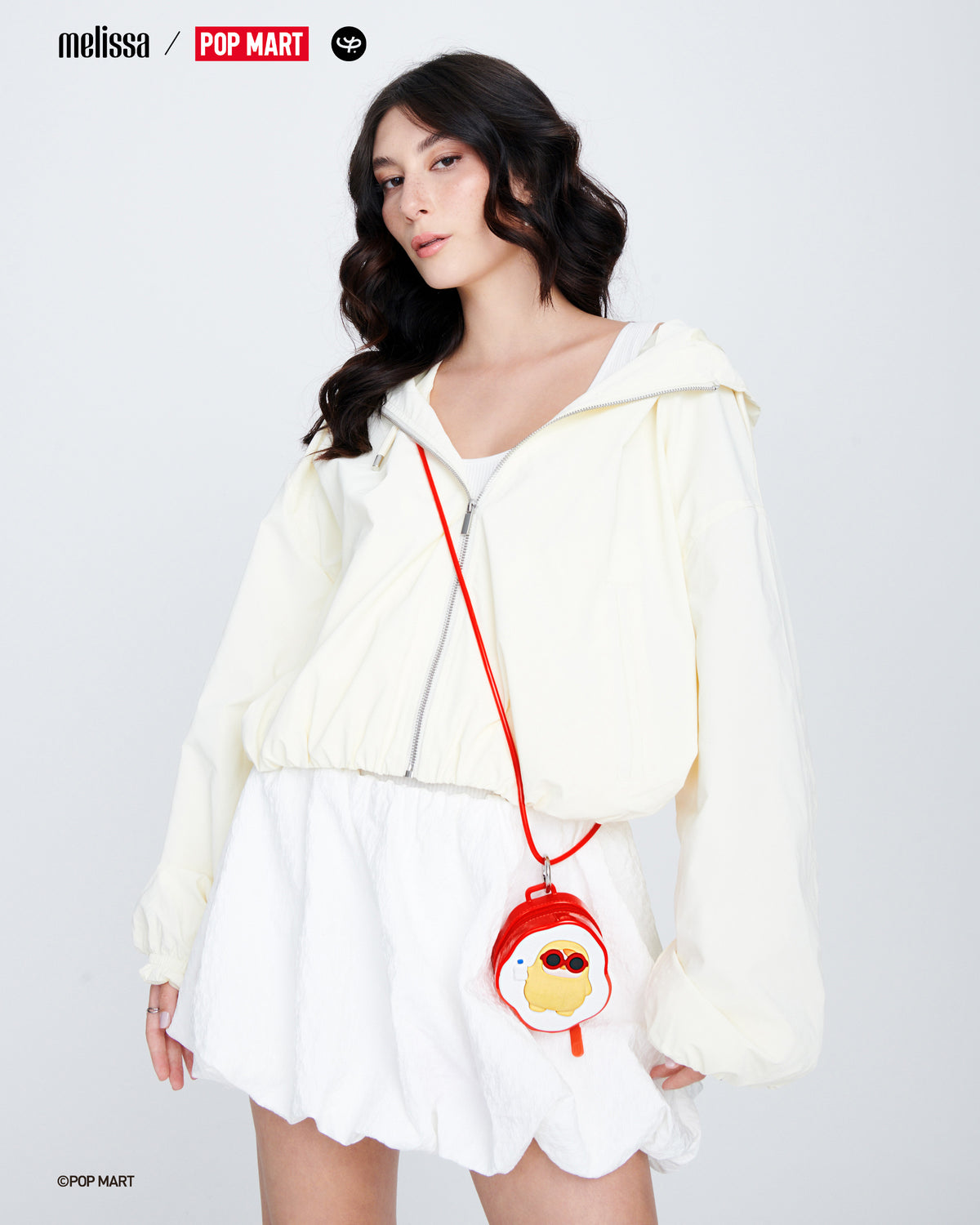 Model in a white skirt and white zipper hoodie wearing a red Melissa Bag + POP MART PUCKY