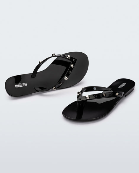 Angled and top view of a pair of black Melissa Harmonic Studs flip flops with gold studs on the upper.