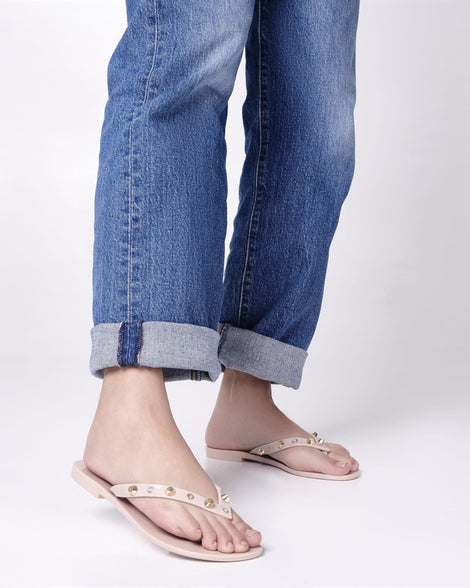 Model's legs in jeans wearing a pair of pink Melissa Harmonic Studs flip flops with gold studs on the upper.