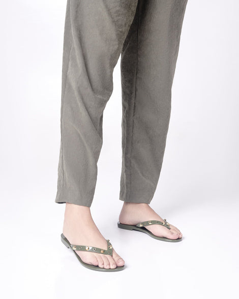 Model's legs in green pants wearing a pair of green Melissa Harmonic Studs flip flops with gold studs on the upper.
