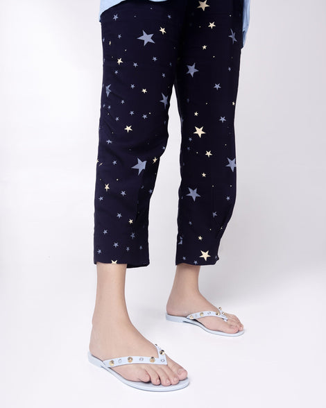 Model's legs in star capris wearing a pair of blue Melissa Harmonic Studs flip flops with gold studs on the upper.