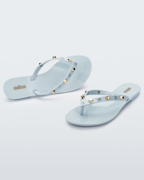 Angled and top view of a pair of blue Melissa Harmonic Studs flip flops with gold studs on the upper.