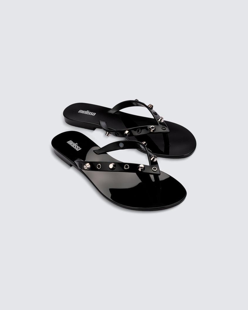 Angled view of a pair of black Melissa Harmonic Studs flip flops with gold studs on the upper.