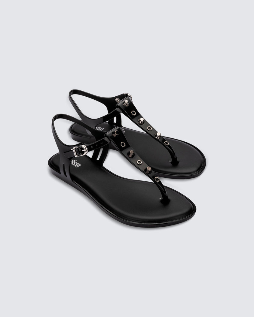 Angled view of a pair of black Melissa Solar studs sandals with gold studded t-strap and gold buckle.