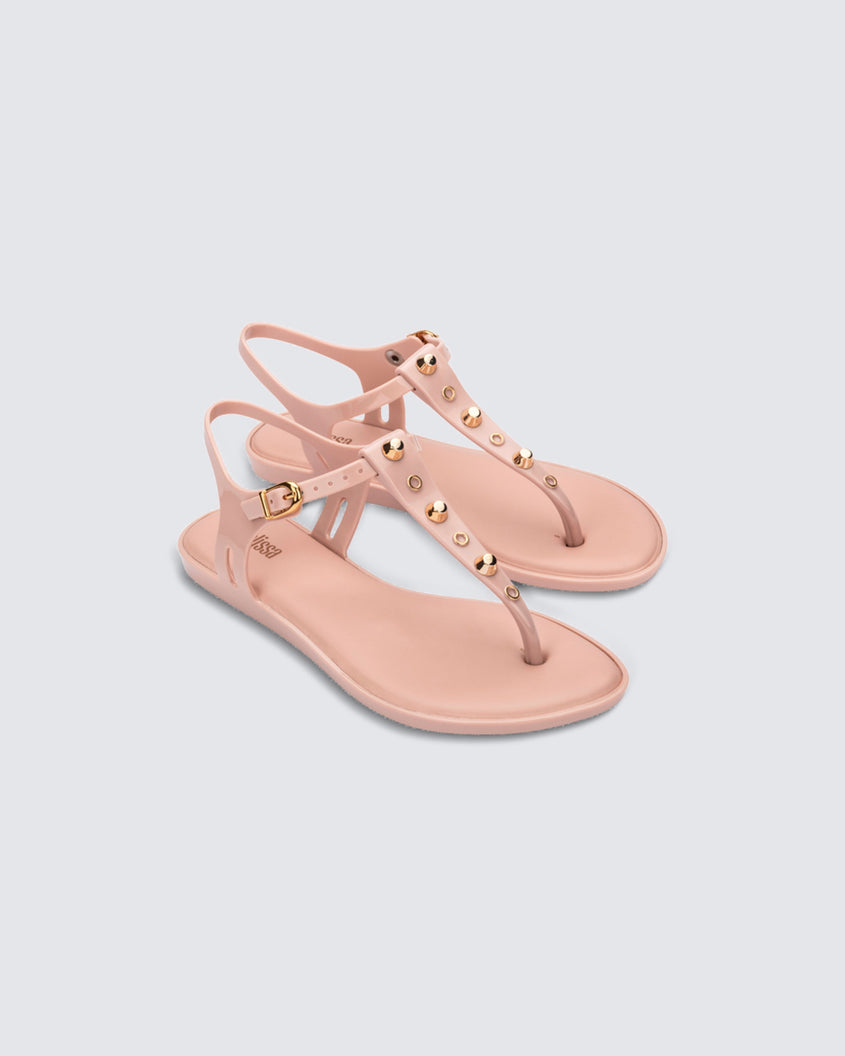 Angled view of a pair of pink Melissa Solar studs sandals with gold studded t-strap and gold buckle.
