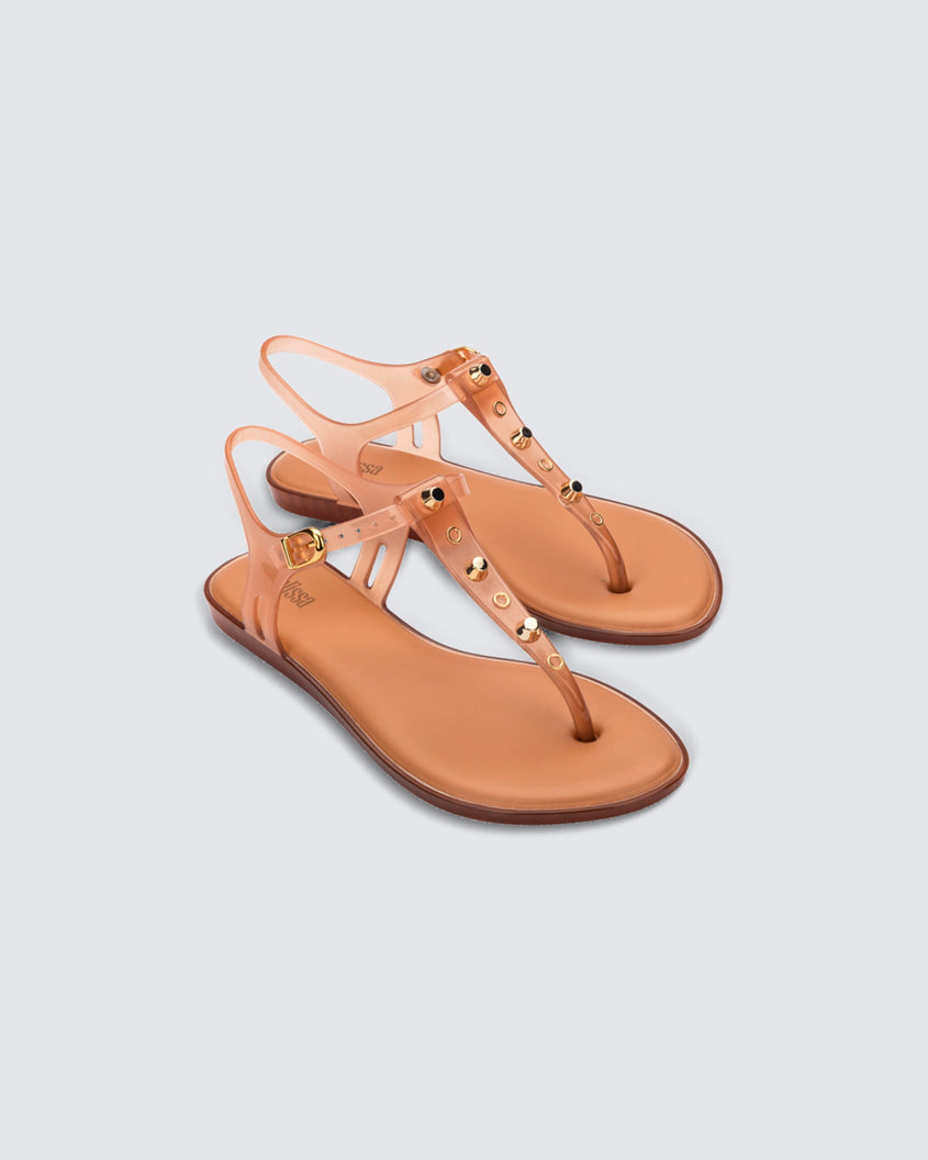 Angled view of a pair of clear beige Melissa Solar studs sandals with gold studded t-strap and gold buckle.