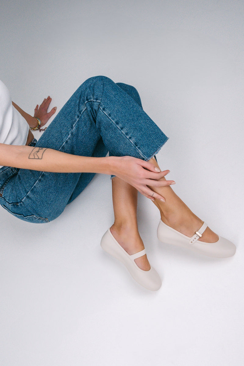 Model's legs in cut off jeans wearing a pair of beige Soft adult flats with strap and gold buckle