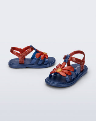 Side and angled view of a pair of glitter blue Hip Bloomy baby sandals with red daisy on top and red straps