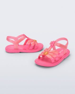 Side and angled view of a pair of glitter pink Hip Bloomy baby sandals with pink daisy on top