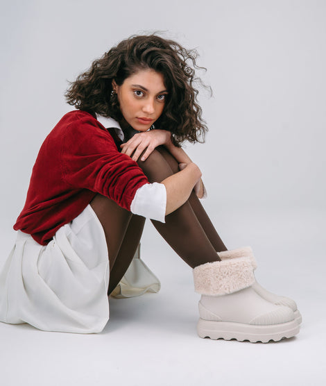 Model in a red sweater, white skirt and brown tights wearing a pair of beige Warm Boot with fuzzy cuff 