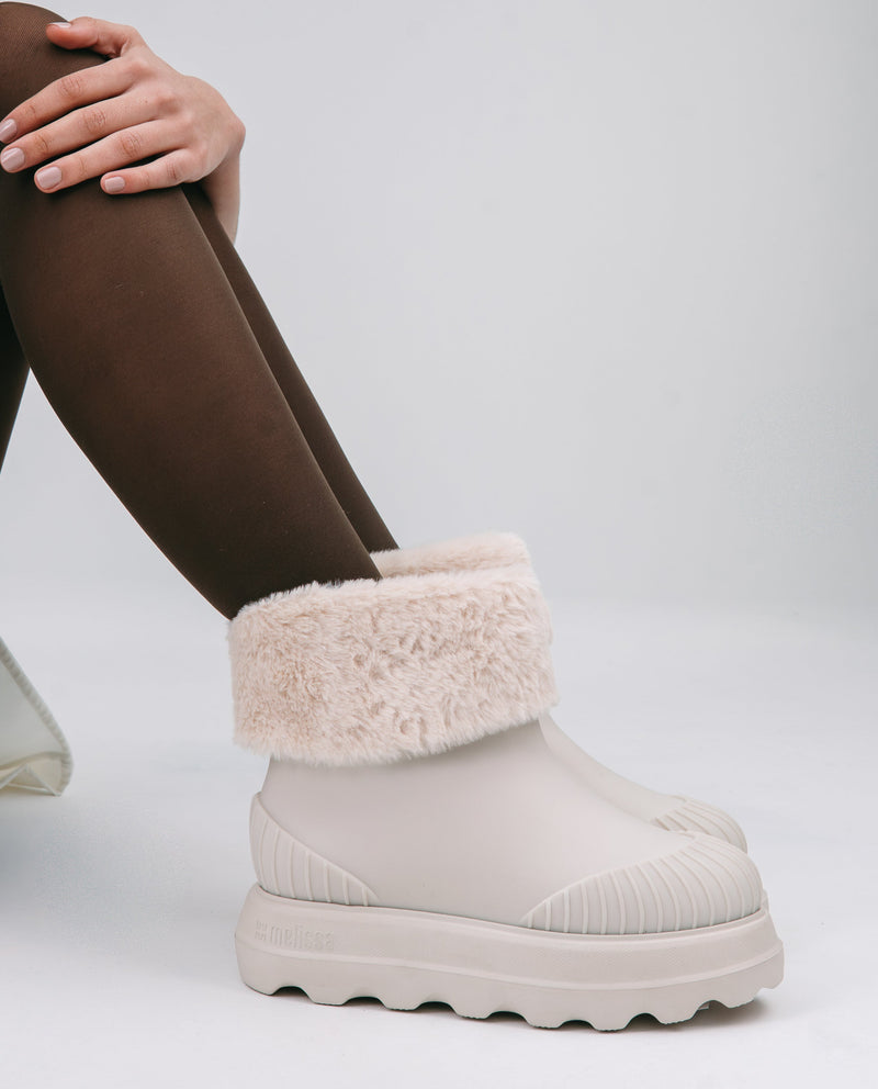 Model's legs in brown tights wearing a pair of beige Warm Boot with fuzzy cuff 