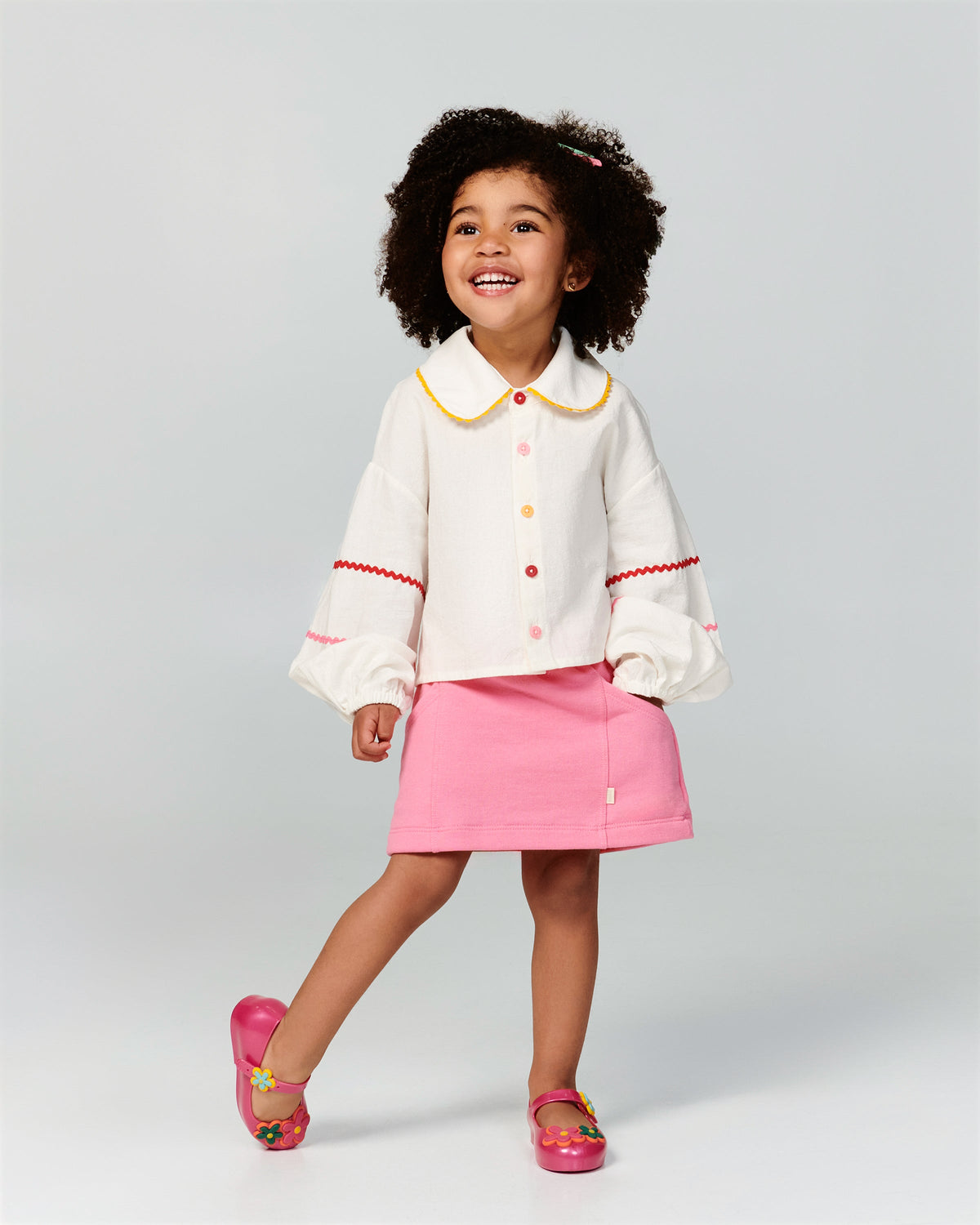 Child model in a white shirt and pink skirt wearing a pair of pink Sweet Love Picnic baby flats with flowers