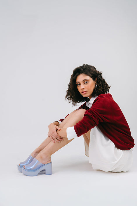 Model in a red sweater and white skirt wearing a pair of pearly blue Mule Hype platforms