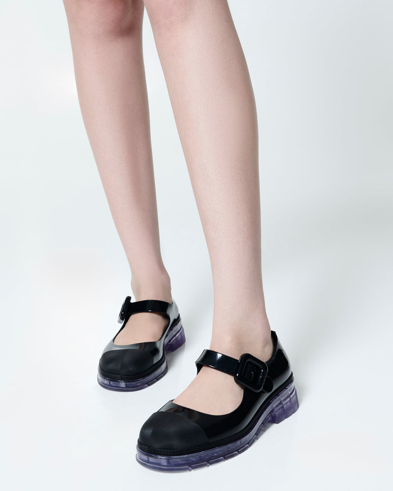 Model's legs wearing  a pair of black with clear sole June mary janes with matte toe cap