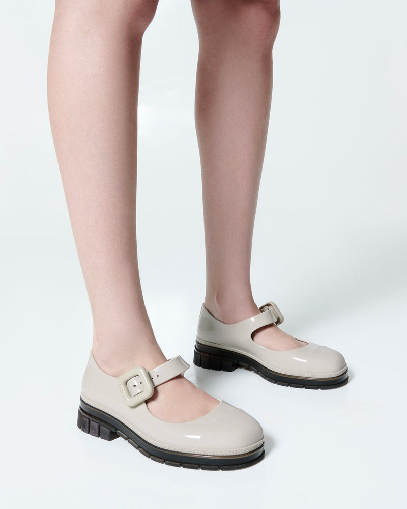 Model's legs wearing  a pair of beige with brown sole June mary janes with matte toe cap