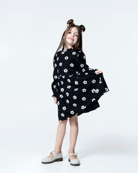 Child model in a black dress with white flowers wearing a pair of beige with brown sole June kids mary janes with matte toe cap