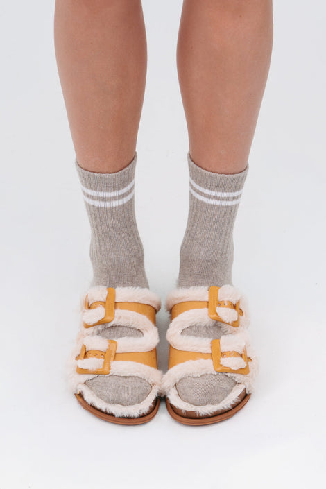 Model's legs in grey socks wearing a pair of orange and beige Cozy Warm Slides