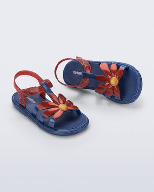 Top and angled view of a pair of glitter blue Hip Bloomy kids sandals with red daisy on top and red straps